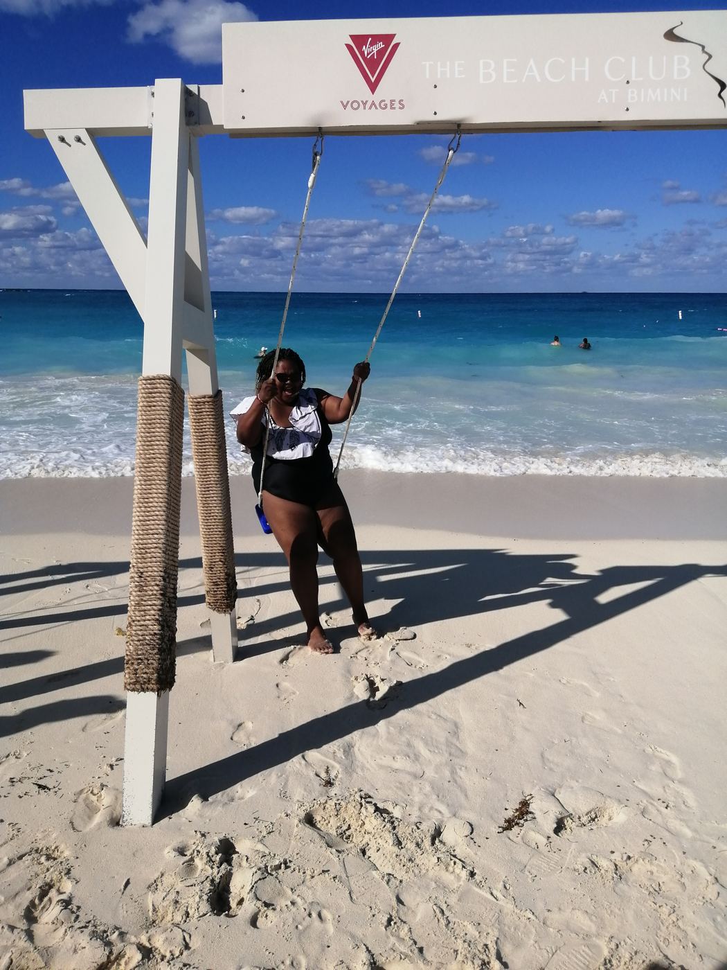 A woman on a rope swing at the beach club in Bimini, turquoise water behind her