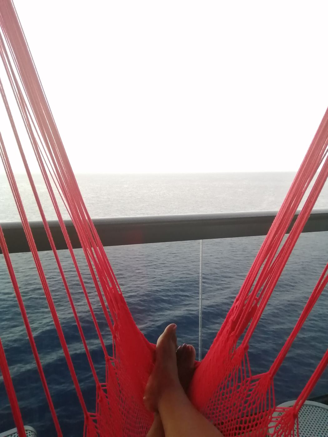 Feet up in a red rope hammock on a ship deck, looking out over open ocean