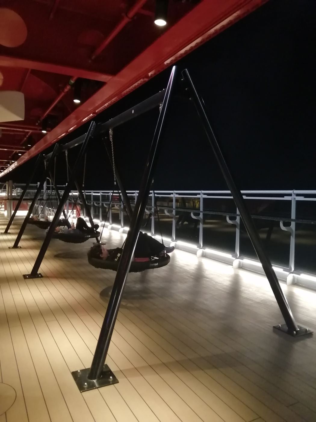 Swings on the ship's deck at night, lit along the rail
